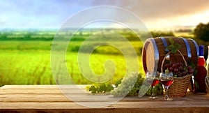 Wine and vineyard in sunset.Colorful grapes in basket. Barrel, red and white wine bottle and glass on wooden table