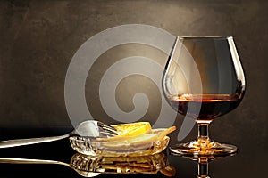 Wineglass of cognac with lemon and fork on glassy table