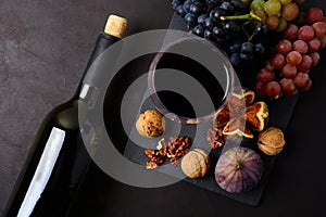 Wineglass with red wine, bottle, grapes, figs and walnuts lying on dark wooden background. Top view.