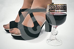 Wineglass with red wine and female feet in high heel shoes.