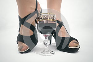 Wineglass with red wine and female feet in high heel shoes.
