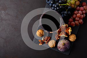 Wineglass with red wine, grapes, figs and walnuts lying on dark wooden background. Top view.
