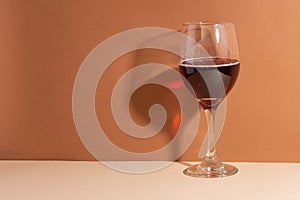 The wineglass with red wine isolated on beige background. The shadow on the wall. The drink of the gods