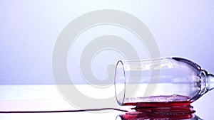 Wineglass tilted down, red wine spilled on the table, white background