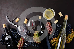 Wineglasses with red and white wine, bottles, grapes, corkscrew and corks lying on dark wooden background