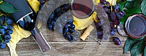 Wineglasses with red wine, bottle, corkscrew, blue grapes, leaves on a wooden table. Wine background with copy space. Top view,