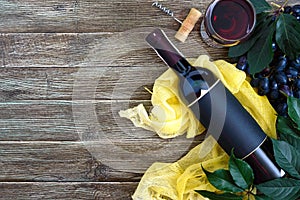 Wineglasses with red wine, bottle, corkscrew, blue grapes, leaves on a wooden table. Wine background with copy space. Top view,
