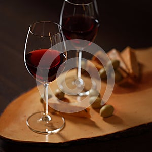 Wineglasses with red wine on wood with cheese and green olives - for cozy home evening