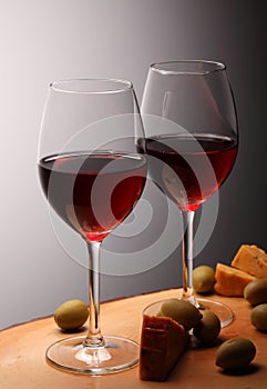 Wineglasses with red wine on wood with cheese and green olives. studio background