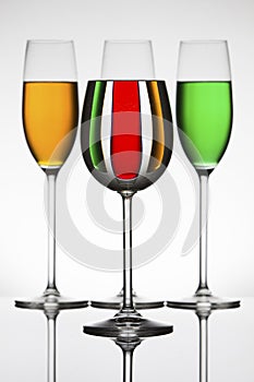 Wineglasses on a shiny surface with different colour fluids that