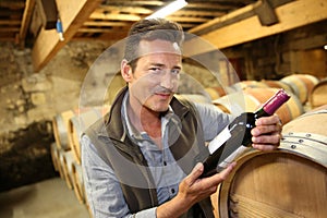 Winegrower in wine cellar with bottle of wine