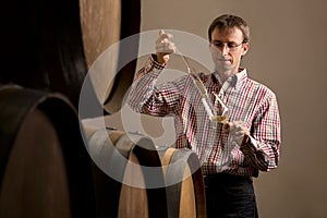 Winemaker in cellar making wine test.