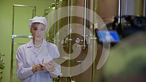 Winemaker woman checking and examining producing wine and presenting with camera in factory.