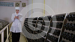 Winemaker young woman checking and examining producing wine at winery in factory.