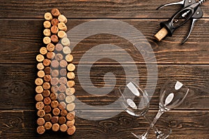 Winery background: bottle shaped corks, corkscrew and two wine glasses on wooden table