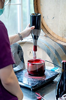 Winery worker hold the wine bottle to dip the bottleneck into wax in the process of seal cap in the factory