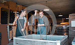 Winery workers making wine with a fruit press tool or equipment in warehouse or distillery. Woman and man winemakers or