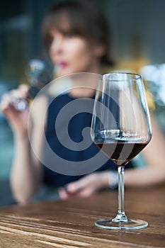 Winetasting concept. Focus on wineglass, woman drinking wine in the background
