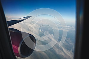 Wing of aircraft with a pink engine against the sky. feathery clouds from window porthole. mood of vacation.