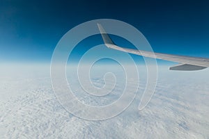 wing of an airplane in flight above clouds in a blue sky