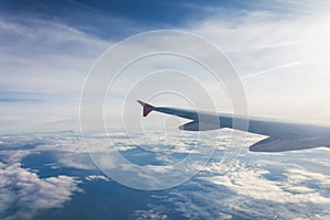 Wing of an airplane flying above the clouds. Looks at the sky from the window of the plane, using airtransport to travel