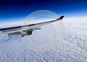 Wing of airplane flying above the clouds in the sky.