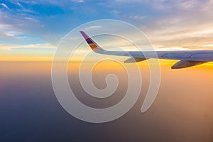 Wing of an airplane flying above the clouds at sunset .