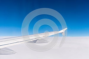 Wing of an airplane flying above the clouds. Window view of the blue sky.