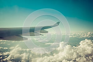 Wing of airplane flying above fluffy clouds.