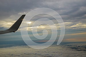 Wing of in airplane flying above the morning clouds in altitude during flight