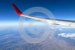 Wing of an airplane flying above the morning clouds and Andean mountain range