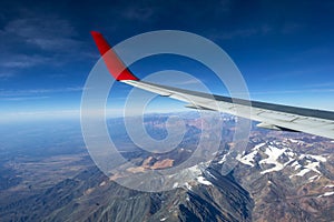 Wing of an airplane flying above the morning clouds and Andean mountain range