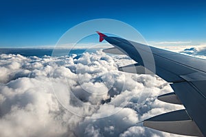 Wing of an airplane flying above the sky with clouds above the ocean