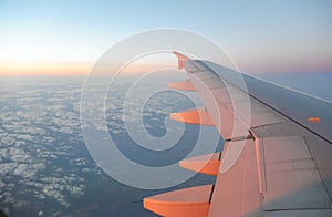 Wing of an airplane flying above the sunrise clouds