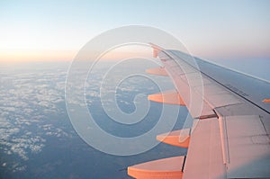 Wing of an airplane flying above the sunrise clouds