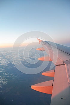 Wing of an airplane flying above the sunrise clouds