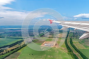 Wing of an airplane flying over a plain area with fields, roads and a town