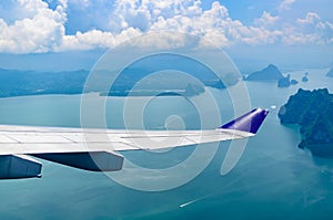 Wing of airplane flying over the sea with cloudy sky.