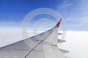 Wing of commercial airplane view from right the window of the plane flying above the clouds on blue sky