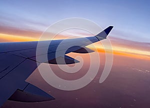 Wing of a commercial wide-body aircraft ascending to cruising altitude. aerial view from a large aircraft at a beautiful orange