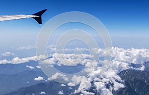 Wing of a Flying Airplane above clouds over Himalayan Mountains