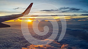 Wing of jet plane over the clouds at high altitude when sunset.