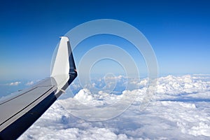 The wing of a passenger plane flying above white clouds