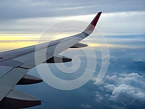 Wing of the plane with cloudy sky on background at sunset