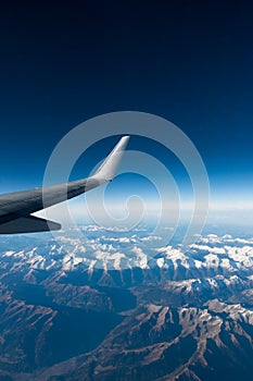 Wing of plane flying over clouds and mountains.