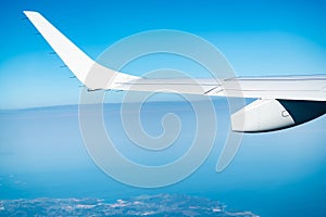 Wing of plane over the city and land. Airplane flying on blue sky. Scenic view from airplane window. Commercial airline flight.