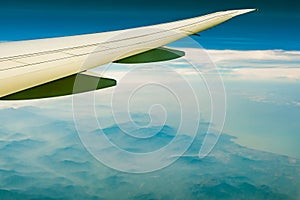 Wing of plane over mountain. Airplane flying on blue sky and white clouds. Scenic view from airplane window. Commercial airline