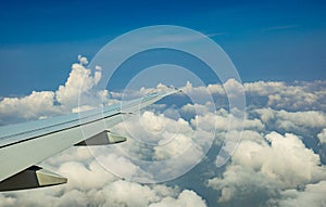 Wing of plane over white clouds. Airplane flying on blue sky. Scenic view from airplane window. Commercial airline flight. Plane