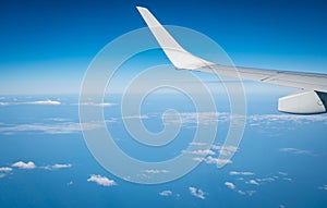 Wing of plane over white clouds. Airplane flying on blue sky. Scenic view from airplane window. Commercial airline flight. Plane