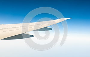 Wing of plane over white clouds. Airplane flying on clear blue sky. Scenic view from airplane window. Commercial airline flight.